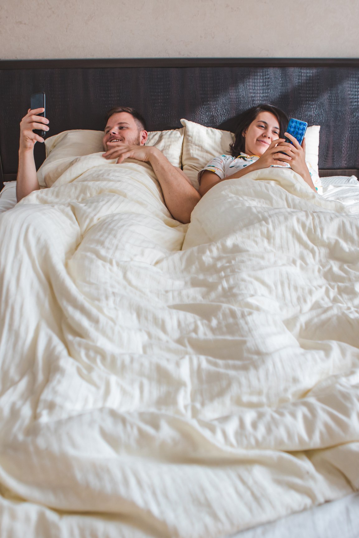 couple laying in bed surfing internet on phone